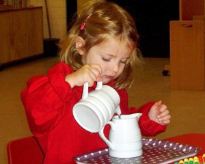 A cute little girl pouring water from one mug to other